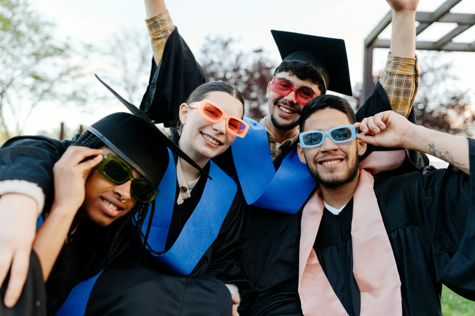 Happy university graduates or prom-goers in caps, gowns, and fun sunglasses, celebrating outdoors.