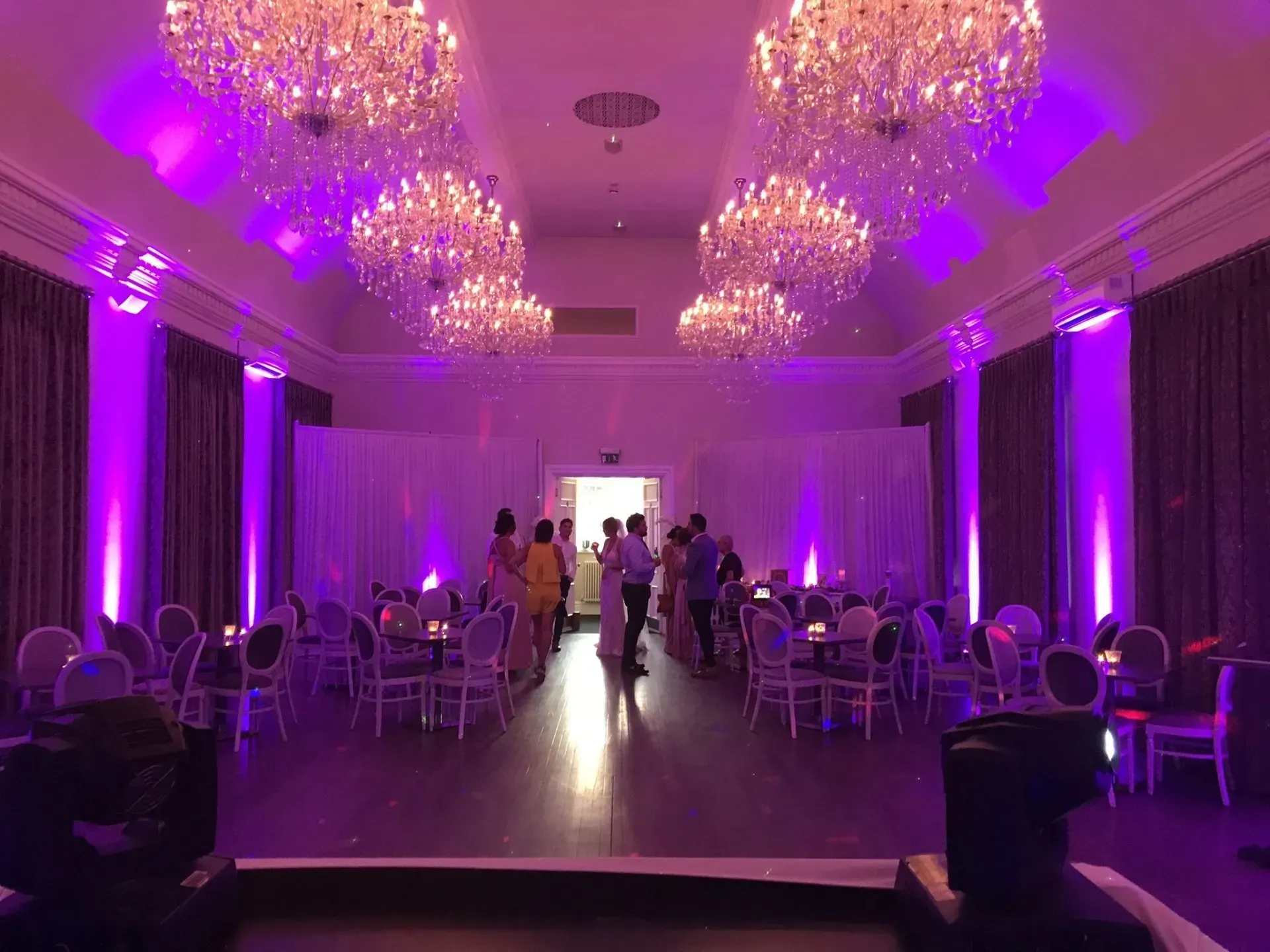 Event venue decorated with purple uplighting, chandeliers, and guests.