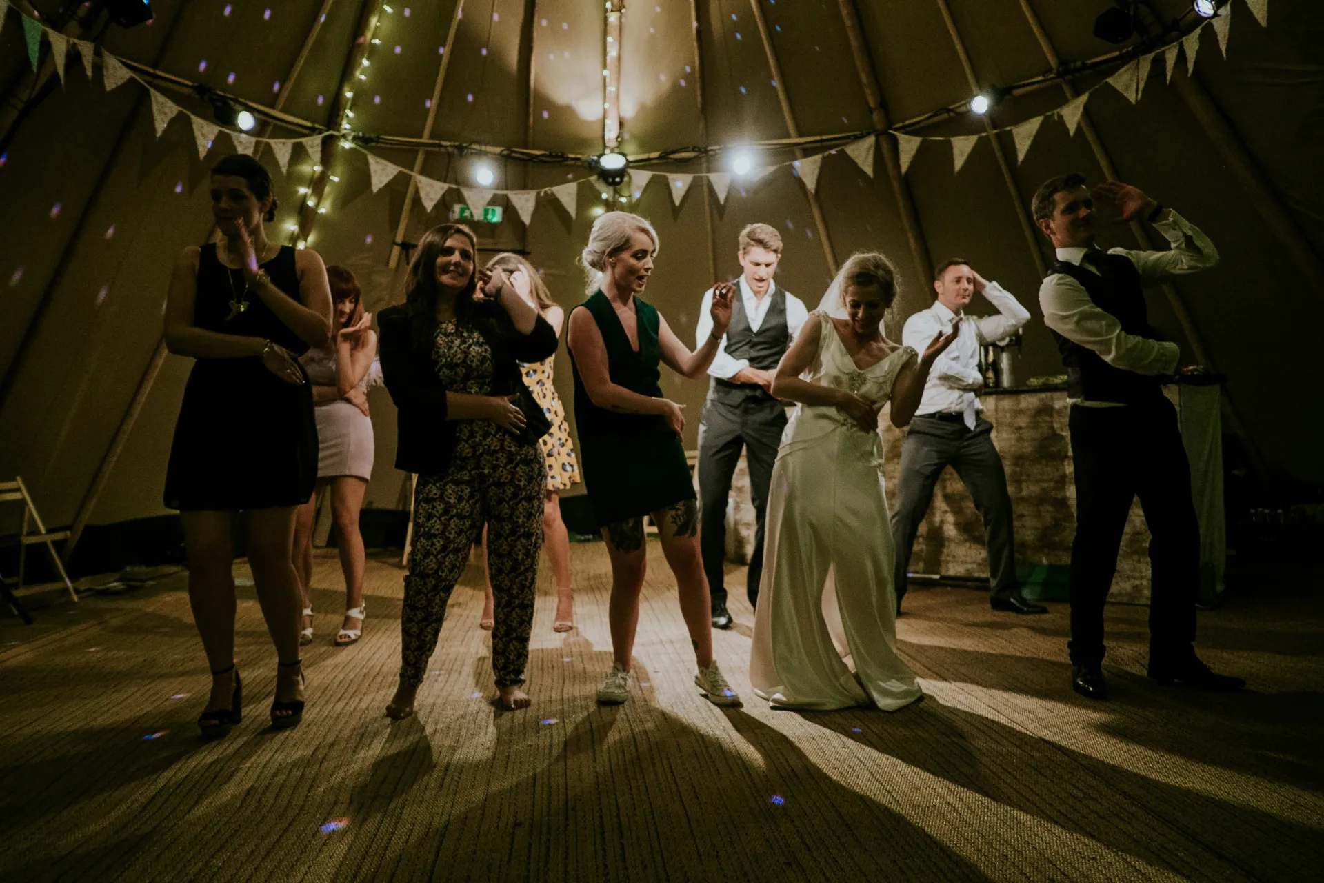 Lively wedding guests dancing at a Tipi reception party with disco lighting.
