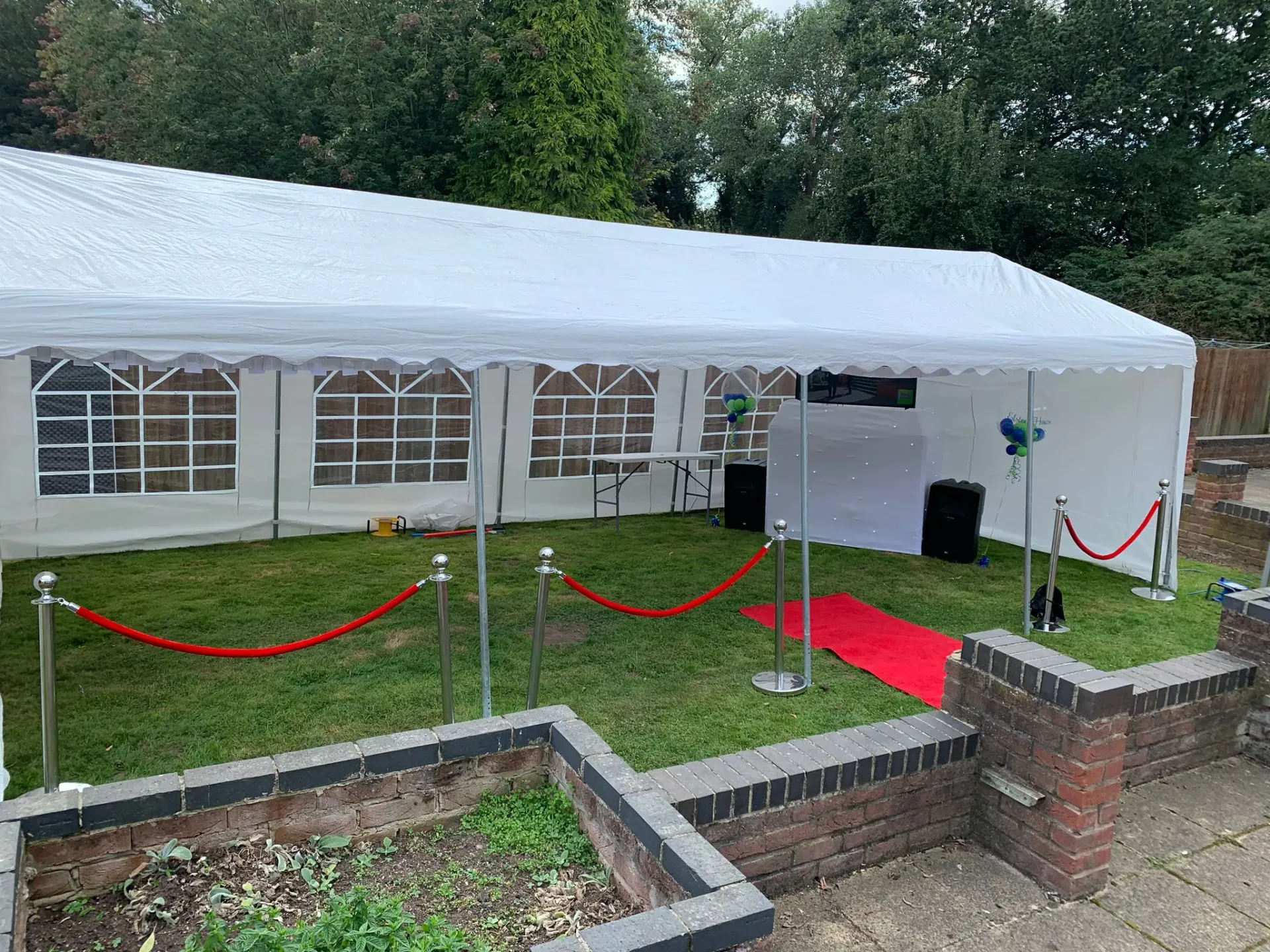 White marquee setup for an outdoor party with red carpet, VIP ropes, and a professional DJ station visible inside.